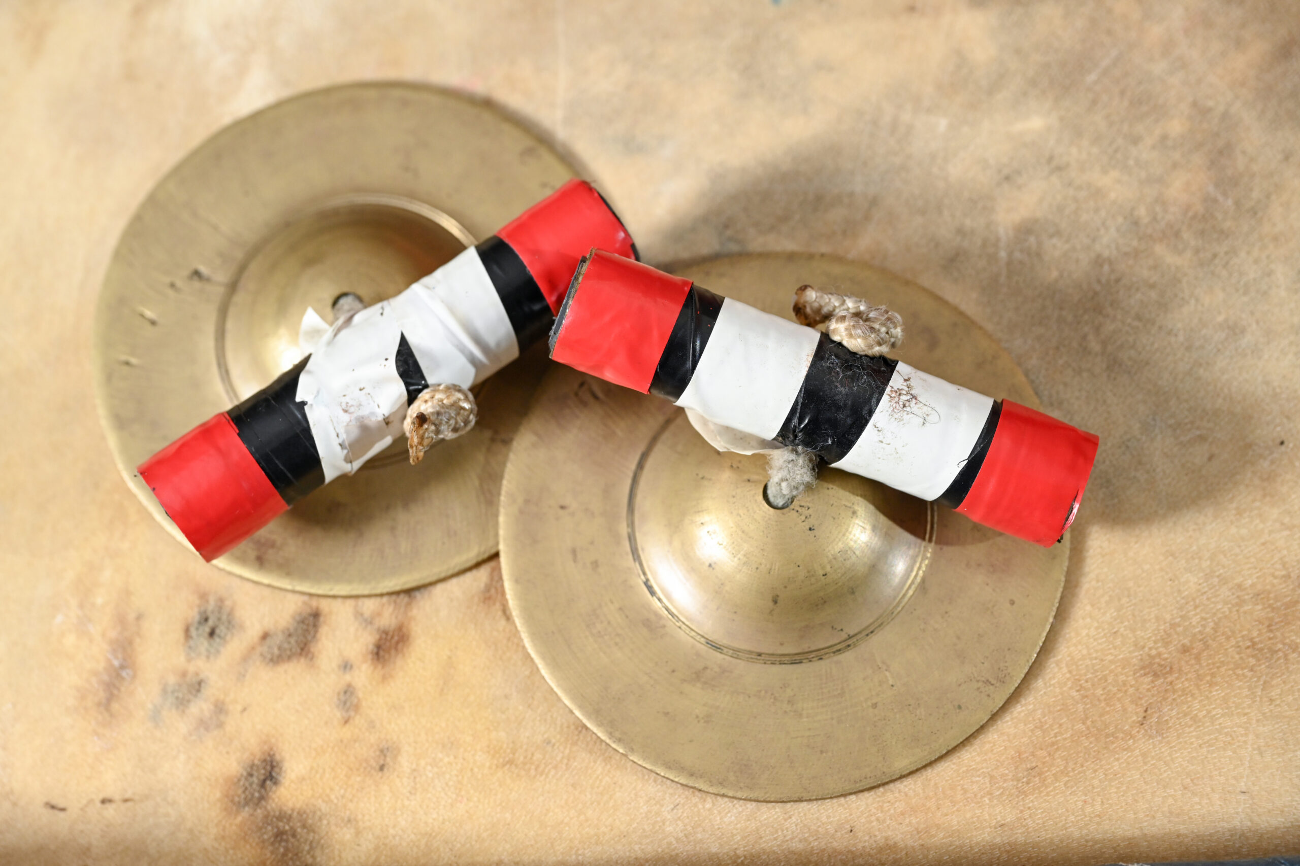 A pair of round cymbals with colorful sticks attached with string as handles.