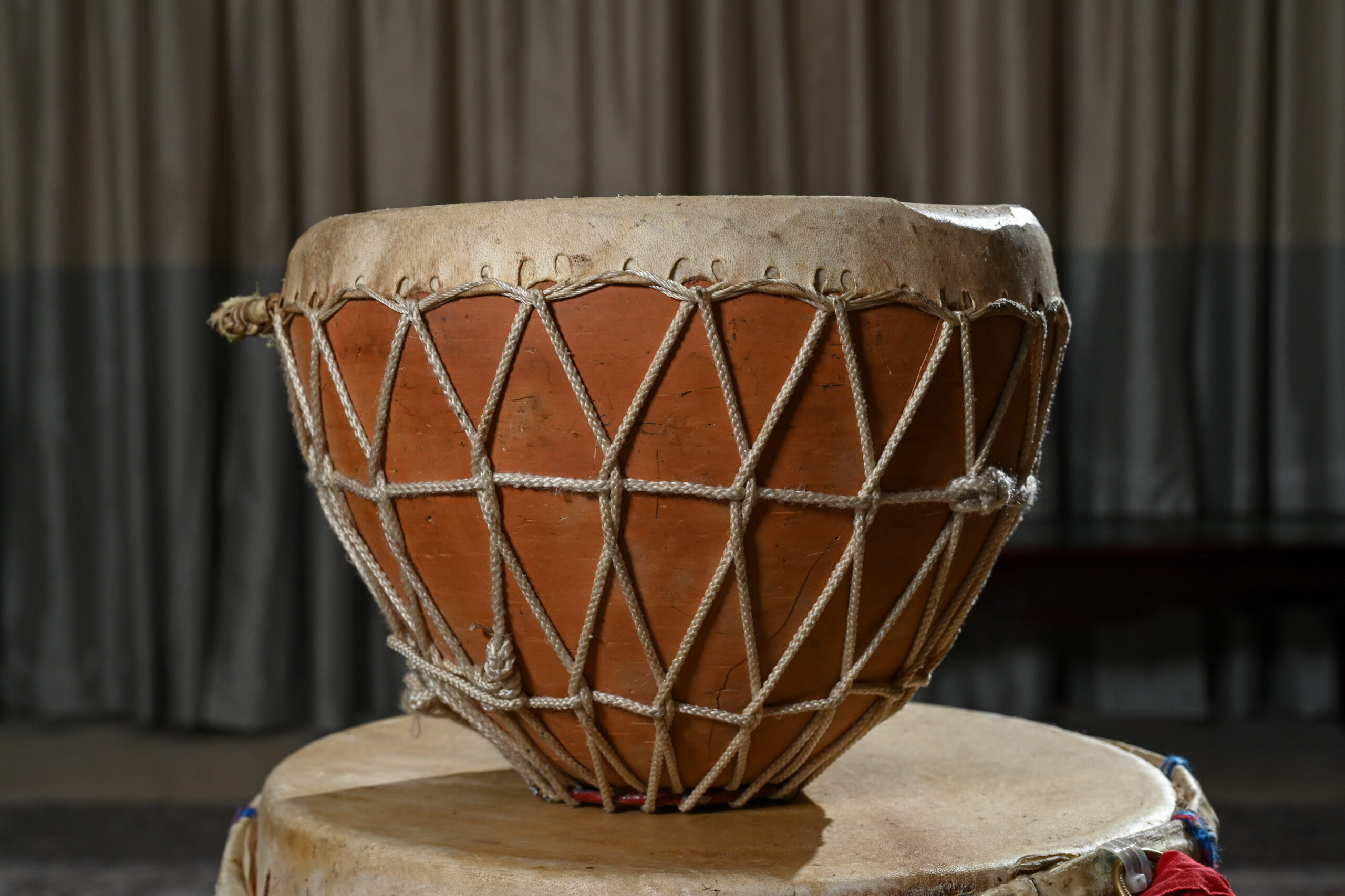 A bowl-shaped drum made with a clay shell and covered in a goat skin head attached to the shell with threaded string along the sides.