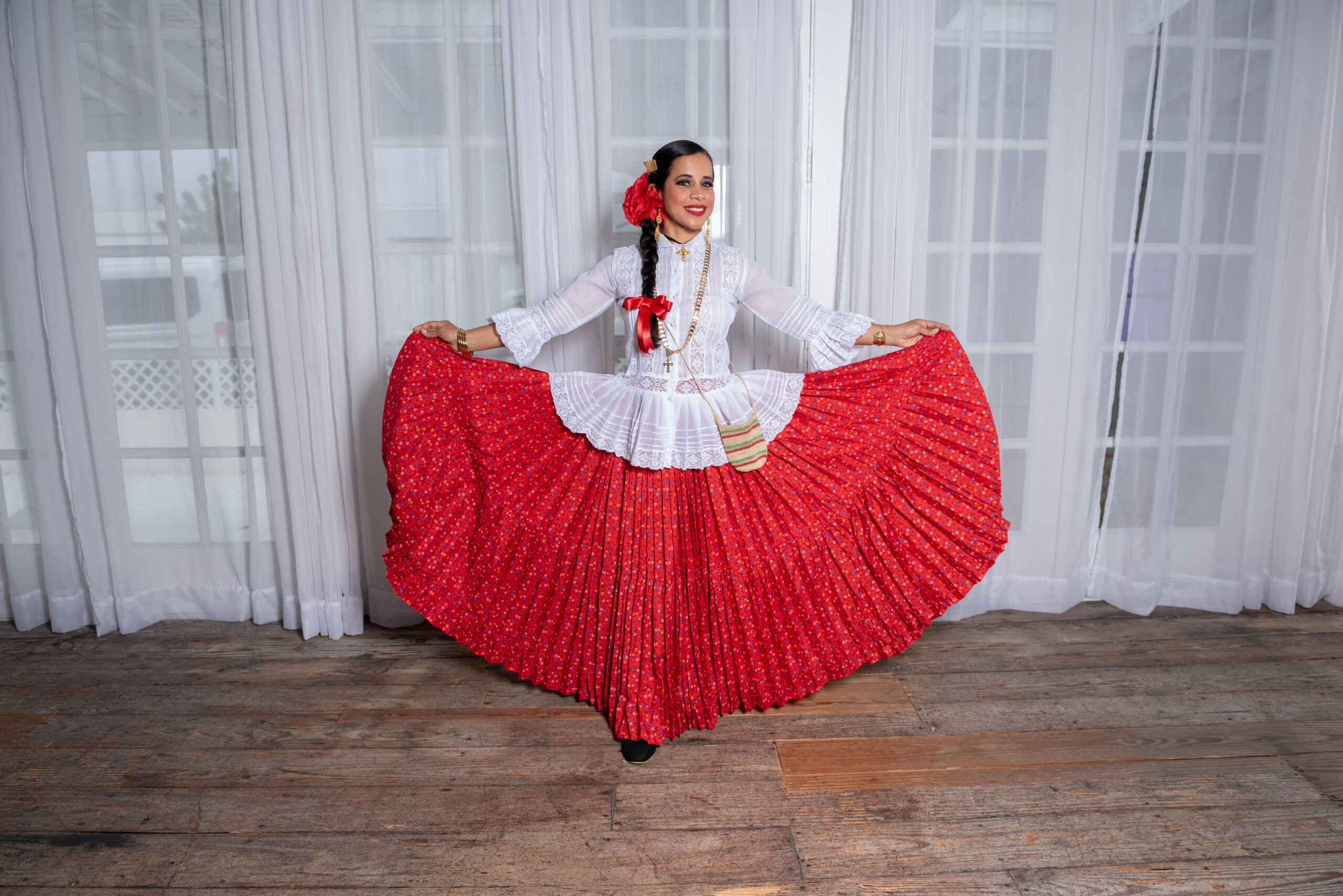 A woman wears a white lace longsleeved top and a red skirt with a red flower in her hair.