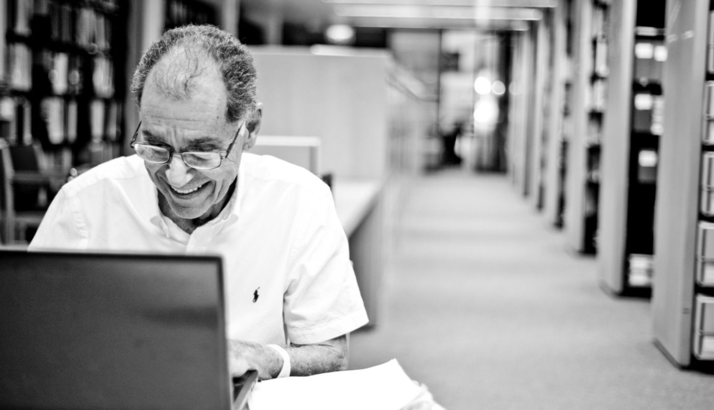 Dr. George sitting in front of a laptop computer in the Museum's Archives and Research Center. Book stacks are visible in the back right of the image.