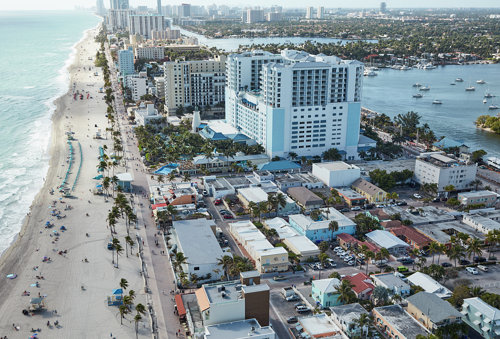 Aerial view of Hollywood Beach looking south. A tall blue and white building can be seen mid-photo and is surrounded by smaller one-story buildings.