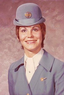 In a formal portrait, a person wears a light blue Pan American Stewardess hat and top with a white dress shirt underneath.