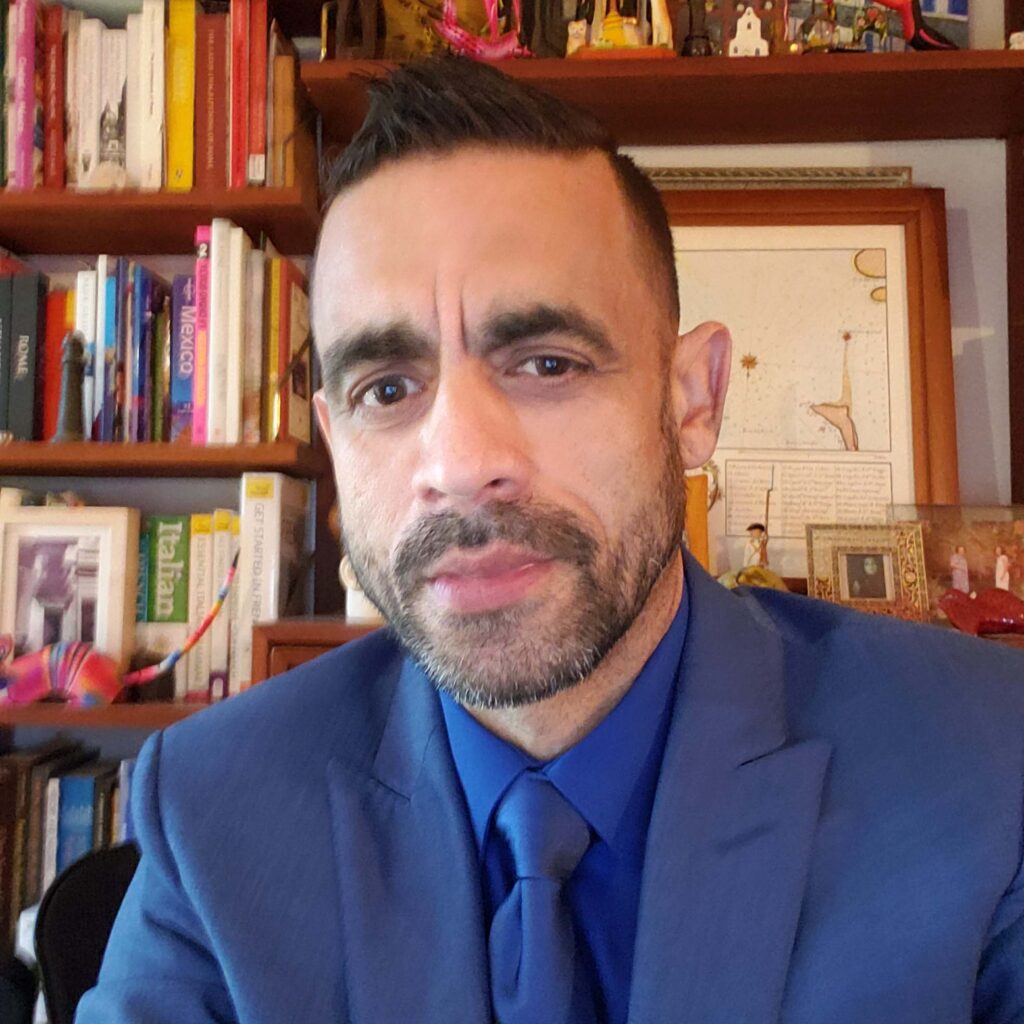 A person wears a blur suit and sits in front of a bookshelf.