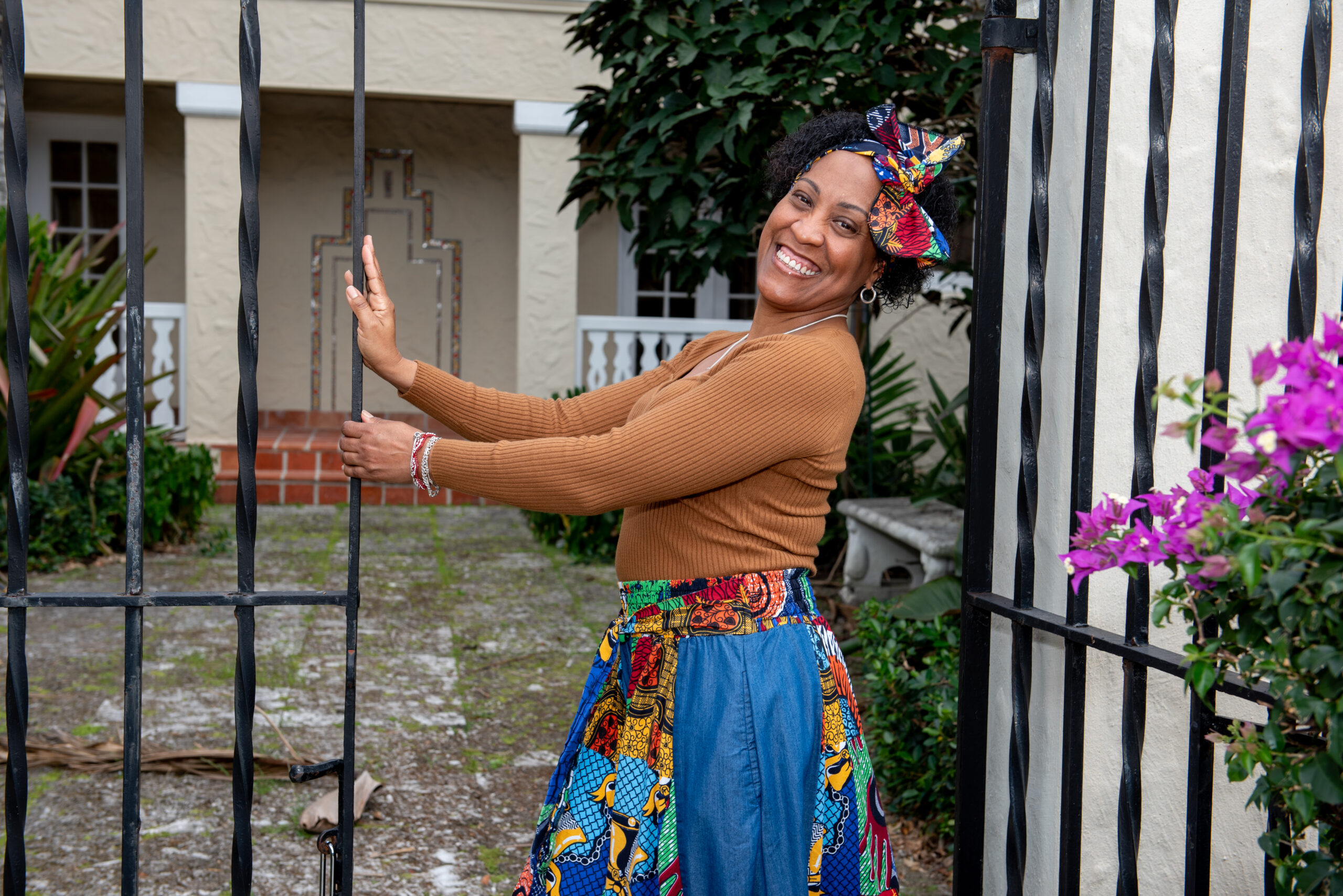 A woman smiles at the camera while posing inside of an iron gate in a garden