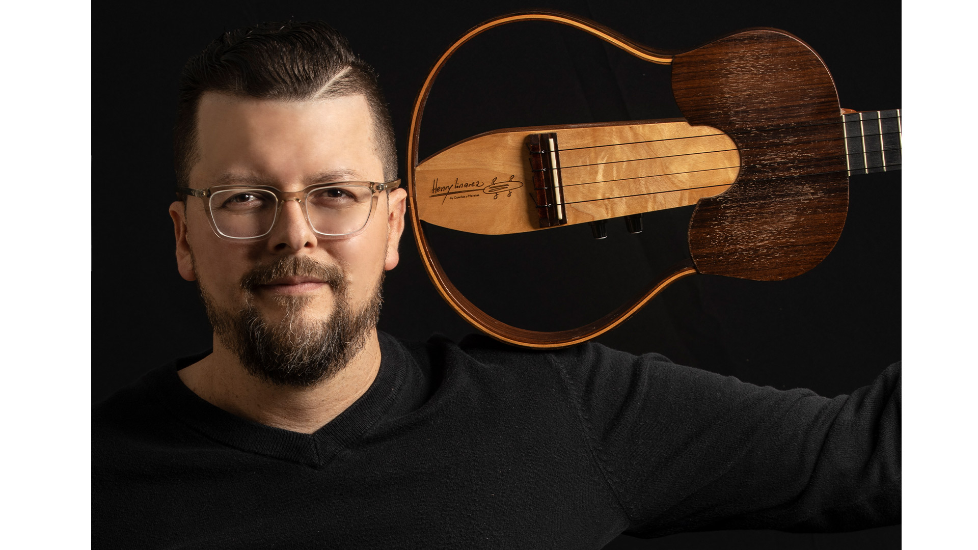 Henry Linarez wears a black shirt and holds his cuatro guitar over his shoulder while looking into the camera