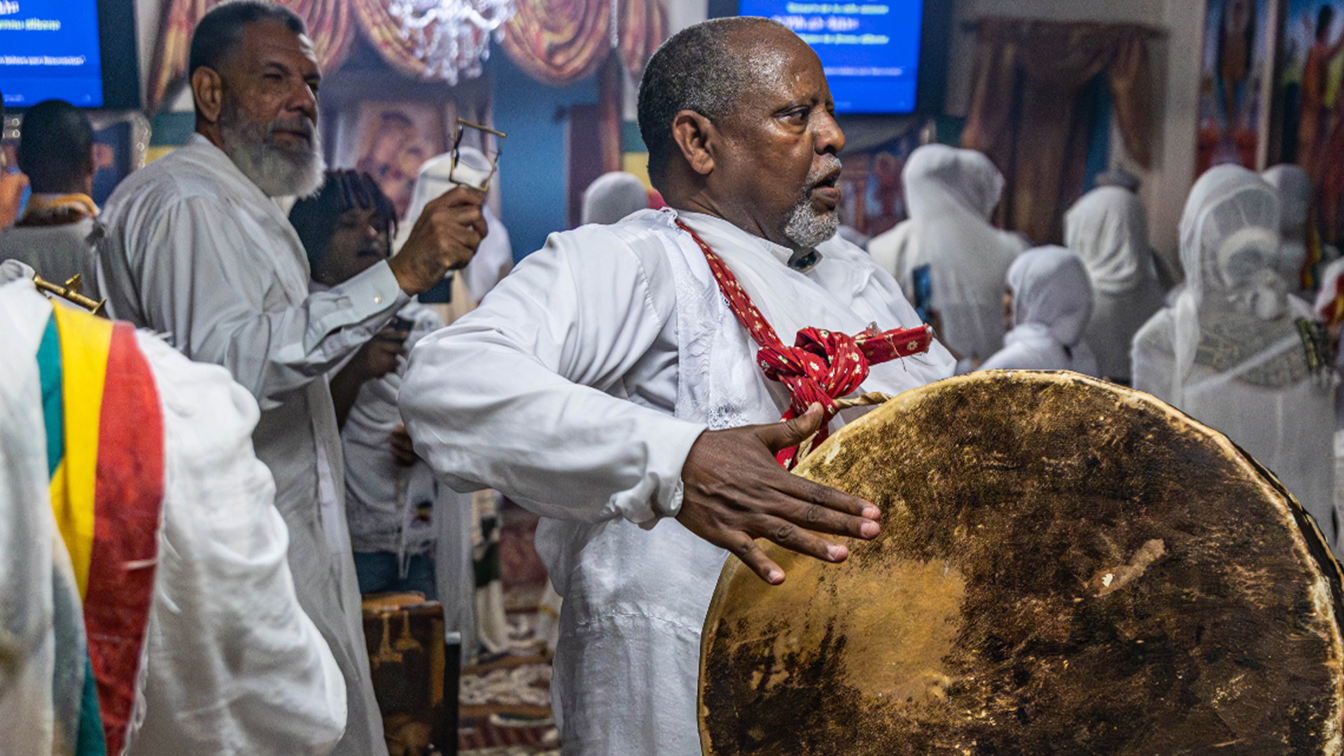 A group of people wearing white play musical instruments in a religious space.