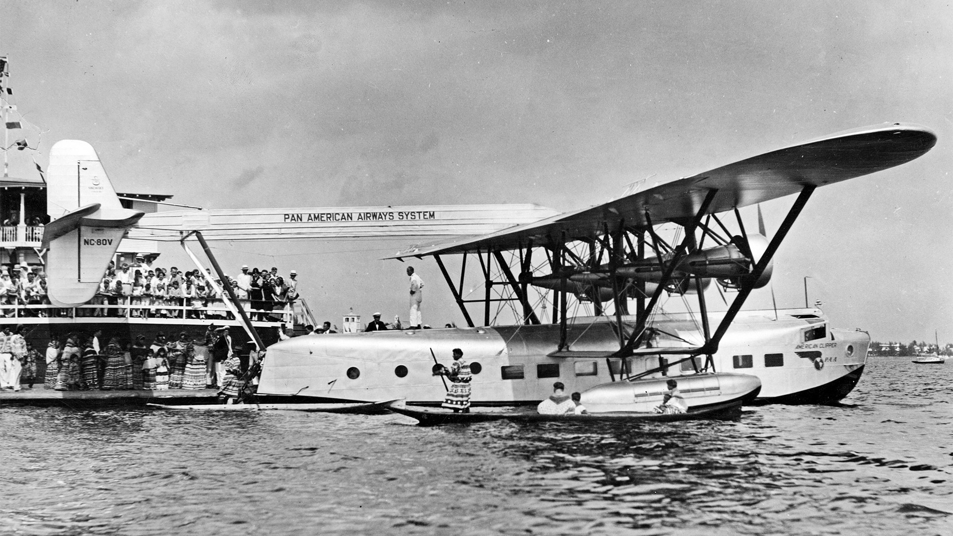 A Pan American Seaplane sits on the water while a crowd looks on.