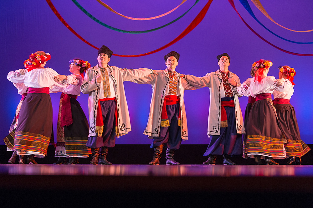 dancers perform on stage. men lock arms while they dance